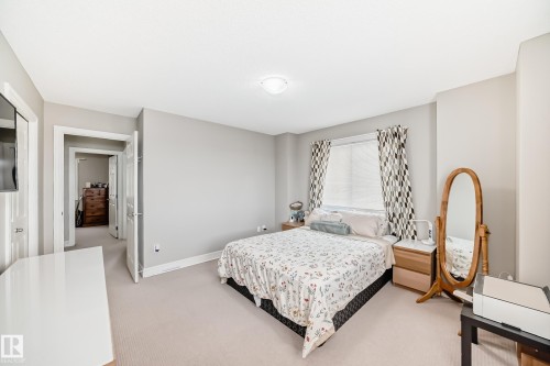 This bedroom features neutral-toned walls, light-colored carpeting, a window with blinds and patterned curtains, and a ceiling light fixture - 138 655 Tamarack Road Nw, Edmonton, AB - Indoor Photo Showing Bedroom