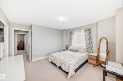 This bedroom features neutral-toned walls, light-colored carpeting, a window with blinds and patterned curtains, and a ceiling light fixture - 