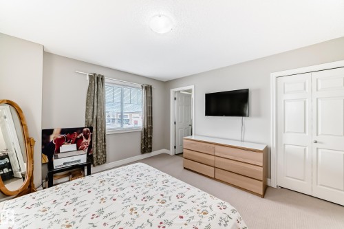 This room features light-colored walls, carpeted flooring, a window with curtains, and a two-door closet - 138 655 Tamarack Road Nw, Edmonton, AB - Indoor Photo Showing Bedroom