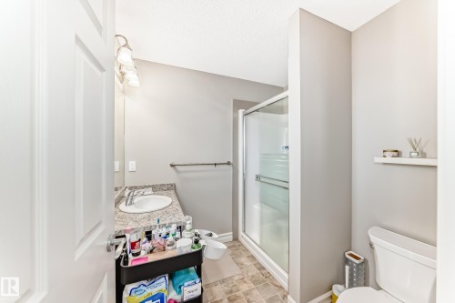 The bathroom features a vanity with a white basin and a speckled countertop, a shower with a sliding glass door, and a toilet - 138 655 Tamarack Road Nw, Edmonton, AB - Indoor Photo Showing Bathroom