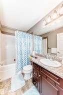 Bathroom featuring a white bathtub, a toilet, a vanity with a white sink, a granite countertop, and a large mirror - 