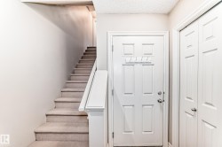 Entryway with a white paneled door, a coat rack, and carpeted stairs with a white banister - 