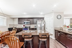 The kitchen features dark wood cabinetry, stainless steel appliances, and a central island with a granite countertop and integrated sink - 