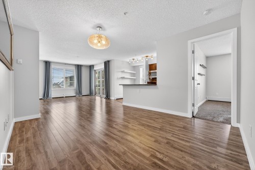 The spacious living area features rich wood-look flooring, large windows, and a decorative ceiling light fixture - 301 1070 Mcconachie Boulevard, Edmonton, AB - Indoor