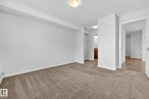 Spacious room featuring neutral carpet flooring, white walls, and an open doorway leading to a hall with hardwood flooring - 301 1070 Mcconachie Boulevard, Edmonton, AB - Indoor Photo Showing Other Room