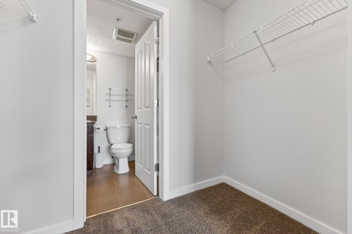 The property features a closet with white wire shelving, and a bathroom with a white toilet, a vanity with a dark brown cabinet, and a mirror - 301 1070 Mcconachie Boulevard, Edmonton, AB - Indoor Photo Showing Bathroom