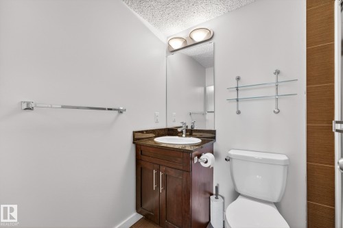 The bathroom features a vanity with a dark wood cabinet and a dark-toned countertop, a white sink with a chrome faucet, and a wall-mounted mirror with overhead lighting - 301 1070 Mcconachie Boulevard, Edmonton, AB - Indoor Photo Showing Bathroom
