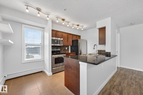 The kitchen features stainless steel appliances, dark wood cabinetry, and a dark stone countertop - 301 1070 Mcconachie Boulevard, Edmonton, AB - Indoor Photo Showing Kitchen