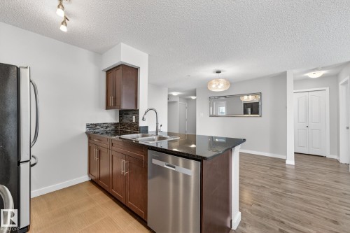 The kitchen features dark wood cabinetry, a dark granite countertop, a stainless steel dishwasher, and a black refrigerator - 301 1070 Mcconachie Boulevard, Edmonton, AB - Indoor Photo Showing Kitchen With Double Sink