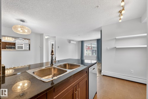 The kitchen features dark countertops, a double stainless steel sink, and wood cabinetry - 301 1070 Mcconachie Boulevard, Edmonton, AB - Indoor Photo Showing Kitchen With Double Sink
