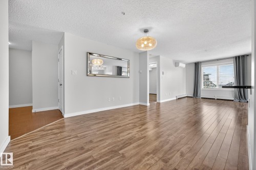 The living area features hardwood flooring, a modern light fixture, and a window with blinds and drapes - 301 1070 Mcconachie Boulevard, Edmonton, AB - Indoor