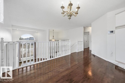 This space features rich, dark hardwood flooring, white balustrade railings, and a decorative chandelier - 3772 30 Street, Edmonton, AB - Indoor Photo Showing Other Room