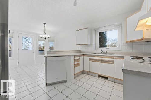 The kitchen features white cabinetry with wood accents, a corner sink with a window view, and a dishwasher - 3772 30 Street, Edmonton, AB - Indoor Photo Showing Kitchen With Double Sink
