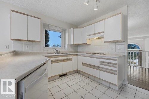 The kitchen features white cabinetry with wood trim, a built-in cooktop, and an integrated sink beneath a window - 3772 30 Street, Edmonton, AB - Indoor Photo Showing Kitchen With Double Sink
