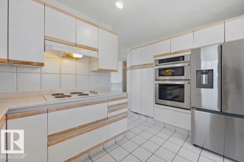 The kitchen features white cabinetry with wood trim, a built-in range, a built-in oven and microwave, and a stainless steel refrigerator - 3772 30 Street, Edmonton, AB - Indoor Photo Showing Kitchen