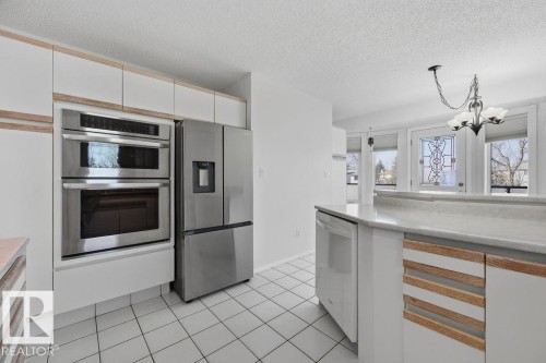 The kitchen features white cabinetry with wood accents, a stainless steel double oven, and a stainless steel refrigerator - 3772 30 Street, Edmonton, AB - Indoor Photo Showing Kitchen