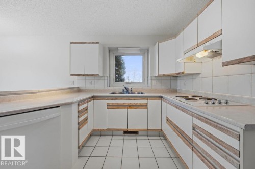 Kitchen featuring white cabinetry with wood trim, white tile flooring, and a built-in electric stovetop - 3772 30 Street, Edmonton, AB - Indoor Photo Showing Kitchen With Double Sink