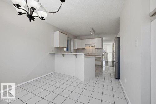 This open-concept area features white tiled flooring and a kitchen with white cabinetry, a light-colored countertop, and a refrigerator - 3772 30 Street, Edmonton, AB - Indoor Photo Showing Kitchen