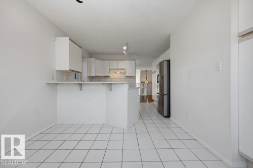 Kitchen featuring white tile flooring, white cabinetry, a breakfast bar, and a stainless steel refrigerator - 3772 30 Street, Edmonton, AB - Indoor Photo Showing Kitchen