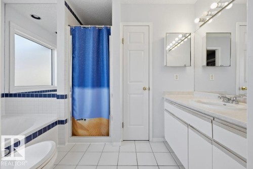The bathroom features a spacious vanity with a single sink and a large mirror, a separate shower area, and a bathtub with tiled surround - 3772 30 Street, Edmonton, AB - Indoor Photo Showing Bathroom