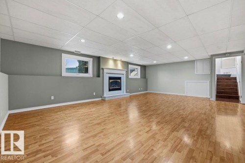 The property features a spacious room with light wood flooring, a fireplace with a white mantel, and recessed lighting - 3772 30 Street, Edmonton, AB - Indoor With Fireplace