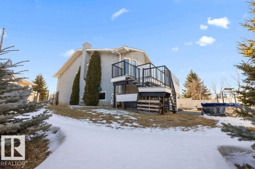 The property features a stucco exterior, a raised deck with dark railings, and a sloped yard with a mix of snow and grass - 3772 30 Street, Edmonton, AB - Outdoor
