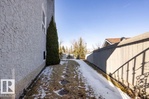 The property features a textured exterior wall, a tall evergreen shrub, and a partial view of a fence - 3772 30 Street, Edmonton, AB - Outdoor