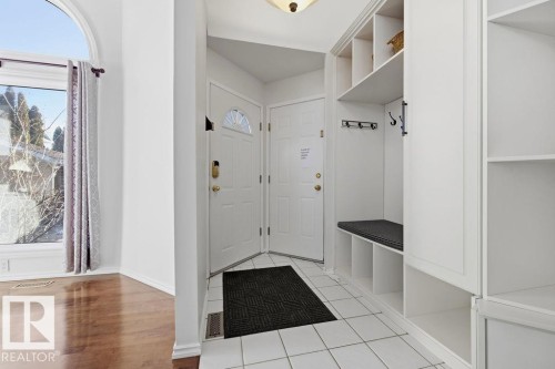 Entryway featuring white tile flooring, a built-in storage unit with shelving and hooks, and a bench with a cushion - 3772 30 Street, Edmonton, AB - Indoor Photo Showing Other Room