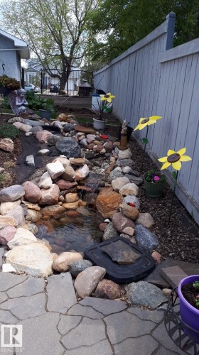 The property features a rock-lined water feature with visible water, bordered by a stone patio - 3772 30 Street, Edmonton, AB - Outdoor With Deck Patio Veranda