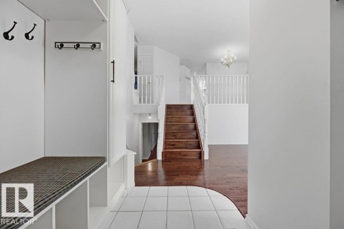 Entryway featuring built-in storage with coat hooks, a tiled floor, and hardwood stairs leading to a lower level and upper landing with a white railing - 3772 30 Street, Edmonton, AB - Indoor