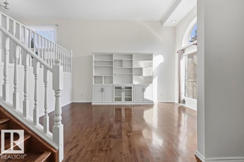 The property features hardwood floors, a built-in white shelving unit, and a white staircase with wooden steps - 3772 30 Street, Edmonton, AB - Indoor Photo Showing Other Room