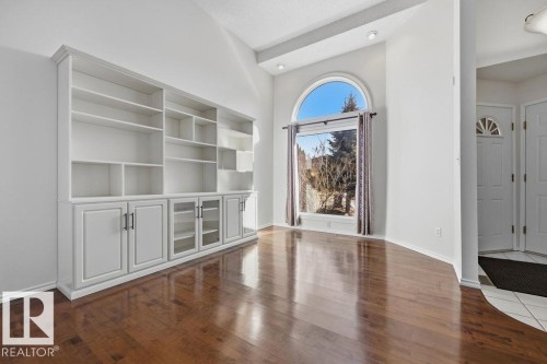 Living area featuring rich hardwood floors, an expansive arched window, and built-in shelving with cabinet storage - 3772 30 Street, Edmonton, AB - Indoor Photo Showing Other Room