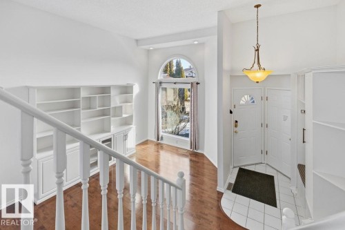 The property features a bright entranceway with a white paneled door and a decorative hanging light fixture, opening to a spacious area with hardwood flooring and a large arched window - 3772 30 Street, Edmonton, AB - Indoor Photo Showing Other Room