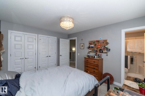 This bedroom features a stylish chandelier, two sets of white bi-fold doors, and a light gray wall color - 7359 179 Avenue, Edmonton, AB - Indoor Photo Showing Bedroom