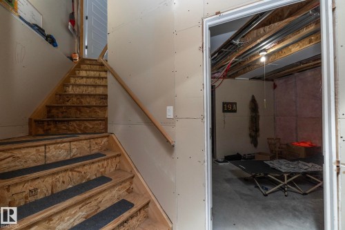 The property features an unfinished staircase with an exposed wood frame and a wooden handrail, leading to an unfinished lower level with exposed ceiling joists - 7359 179 Avenue, Edmonton, AB - Indoor