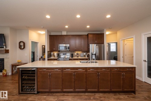 The property features a kitchen with rich wood cabinetry, stainless steel appliances, and a large central island with a light-colored countertop - 307 Ravine Close, Devon, AB - Indoor Photo Showing Kitchen With Double Sink