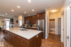 This property features a kitchen with rich wood cabinetry, stainless steel appliances, and a spacious island with a sink and light-colored countertop - 