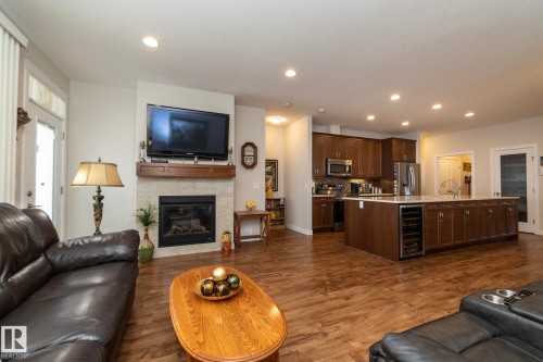 The property features hardwood floors, a fireplace with a stone surround, and an open-concept kitchen with a large island and dark wood cabinetry - 307 Ravine Close, Devon, AB - Indoor Photo Showing Living Room With Fireplace