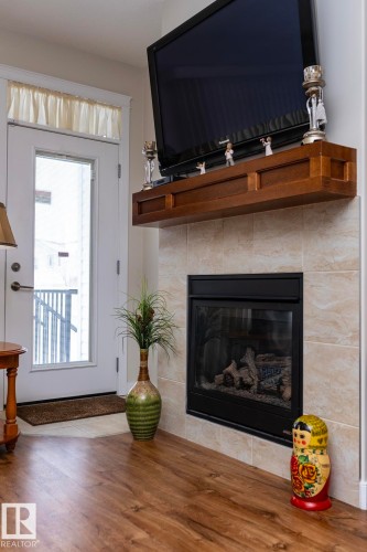 Living area featuring wood-style flooring, a fireplace with a tile surround, and a white exterior door with glass panels - 307 Ravine Close, Devon, AB - Indoor Photo Showing Living Room With Fireplace