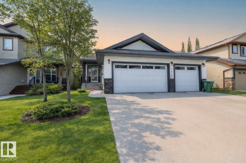 The property features a triple-car garage with white doors, a paved driveway, and a well-maintained lawn with mature trees - 307 Ravine Close, Devon, AB - Outdoor With Facade