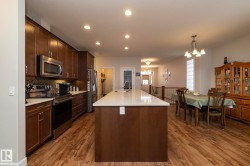 Open-concept kitchen and dining area featuring rich wood cabinetry, stainless steel appliances, a spacious island with a white countertop, and wood-style flooring - 