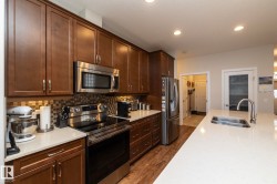 The kitchen features abundant rich wood cabinetry, stainless steel appliances, a tiled backsplash, and a spacious white countertop with an undermount sink - 