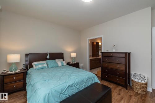 This room features wood-look flooring and a recessed doorway leading to a bathroom with a vanity - 307 Ravine Close, Devon, AB - Indoor Photo Showing Bedroom