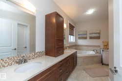 Bathroom featuring a double vanity with stone countertops, dark wood cabinetry, and an integrated corner bathtub with tiled surround - 
