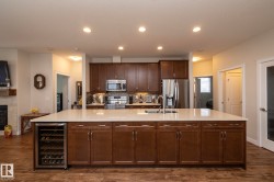 The kitchen features a large island with a light-colored countertop and integrated wine fridge, dark wood cabinetry, and stainless steel appliances - 
