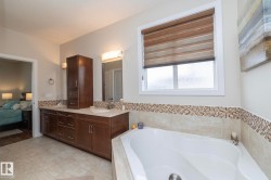 The bathroom features a built-in tub, a double vanity with dark wood cabinetry and light countertops, and tile flooring - 