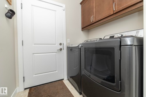 Laundry room featuring light-colored walls, wood-finish cabinetry, and a pair of dark-colored appliances - 307 Ravine Close, Devon, AB - Indoor Photo Showing Laundry Room