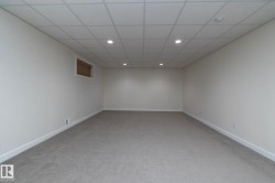 This spacious room features neutral-toned carpet flooring, white walls, and a dropped ceiling with recessed lighting - 