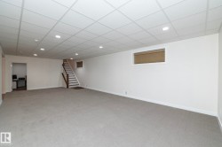 Spacious room featuring light grey carpet, white walls, a grid-patterned ceiling with recessed lighting, and a window with horizontal blinds - 