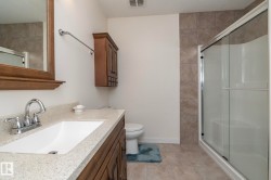 Bathroom featuring a vanity with a light-colored countertop and wooden cabinetry, a shower with a sliding glass door, and tiled flooring - 